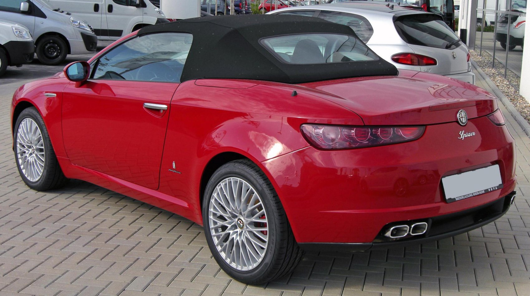 Red convertible with black soft-top, distinctive rear taillights, and quad exhaust tips