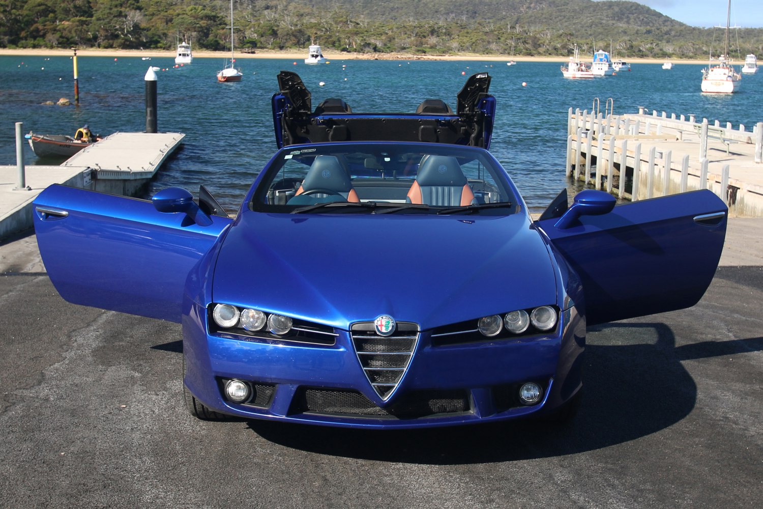 Blue convertible with open doors and retractable roof at marina