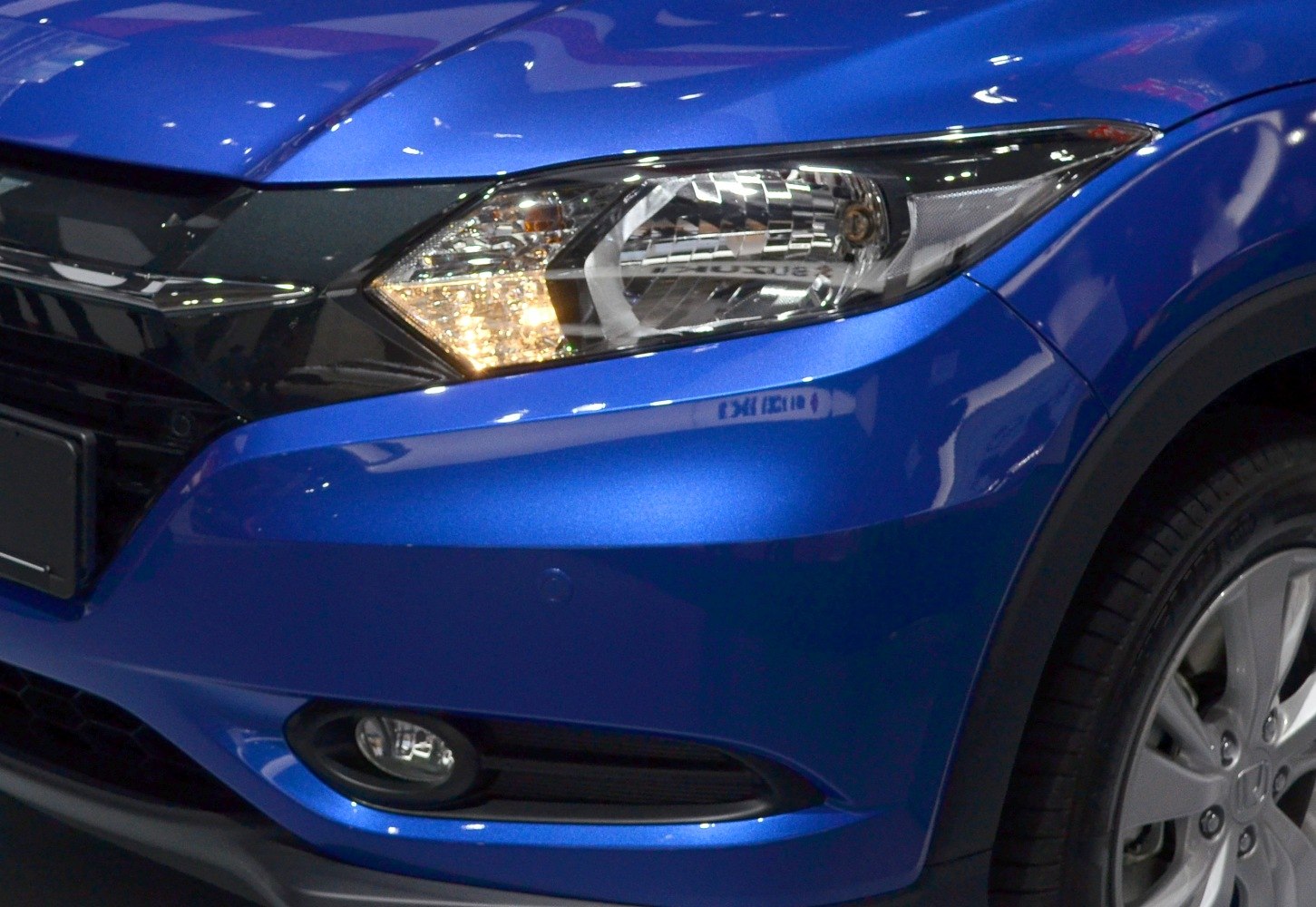 Close-up of car front headlight and fog light with blue bumper and tire