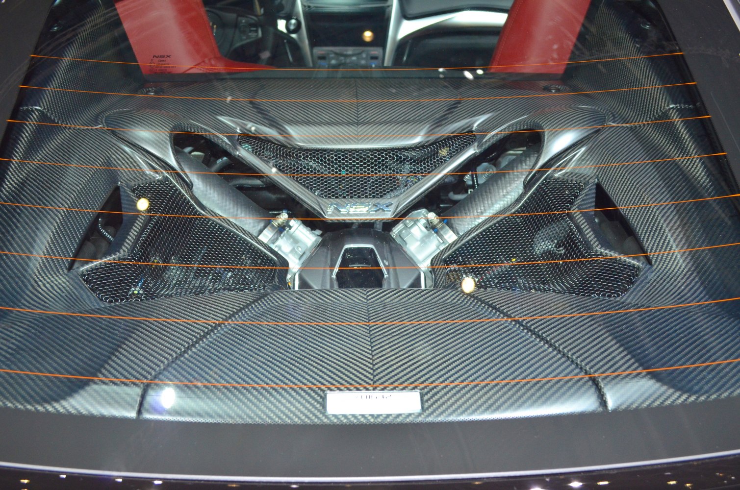 Carbon fiber engine cover with visible engine components under rear glass