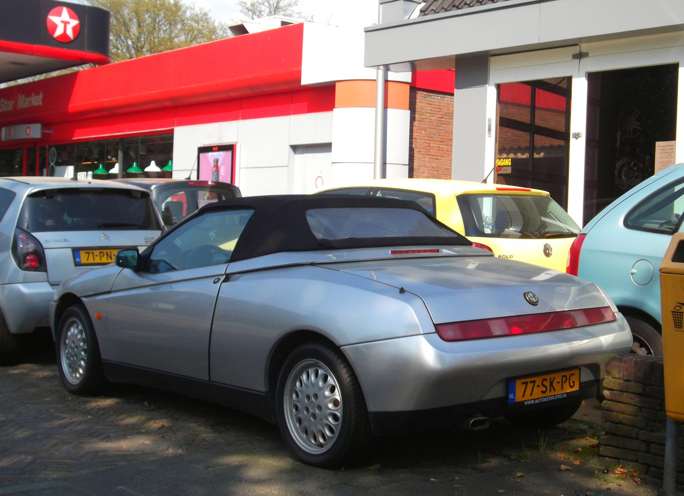 Silver convertible with black soft top and circular hubcap wheels.