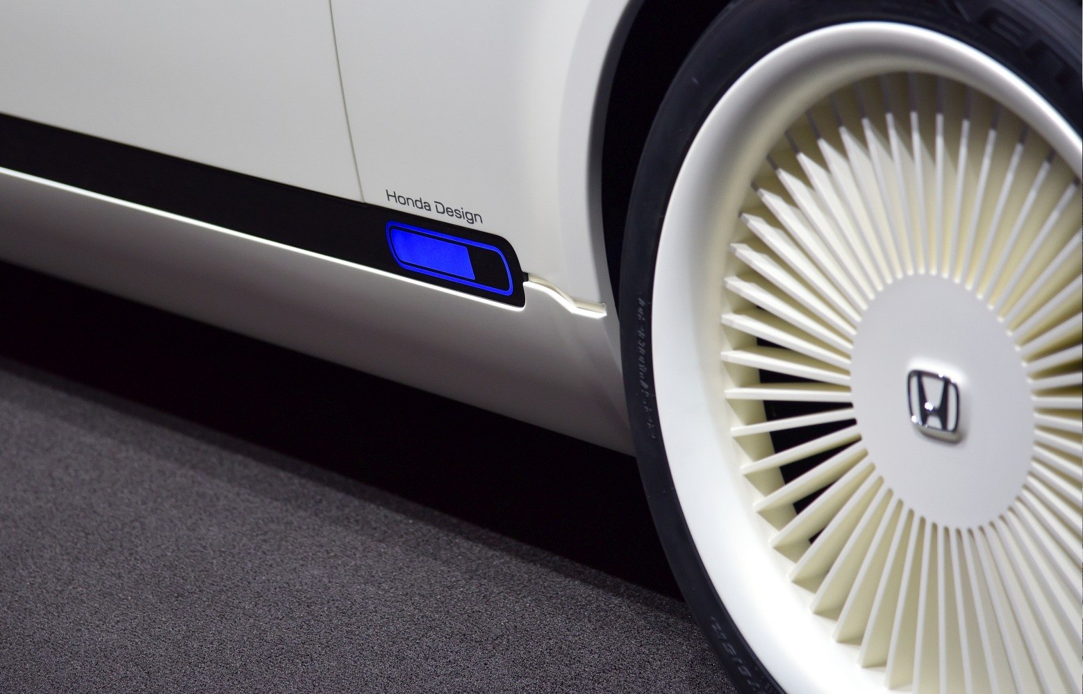 Futuristic wheel design and illuminated charging port on white car side.