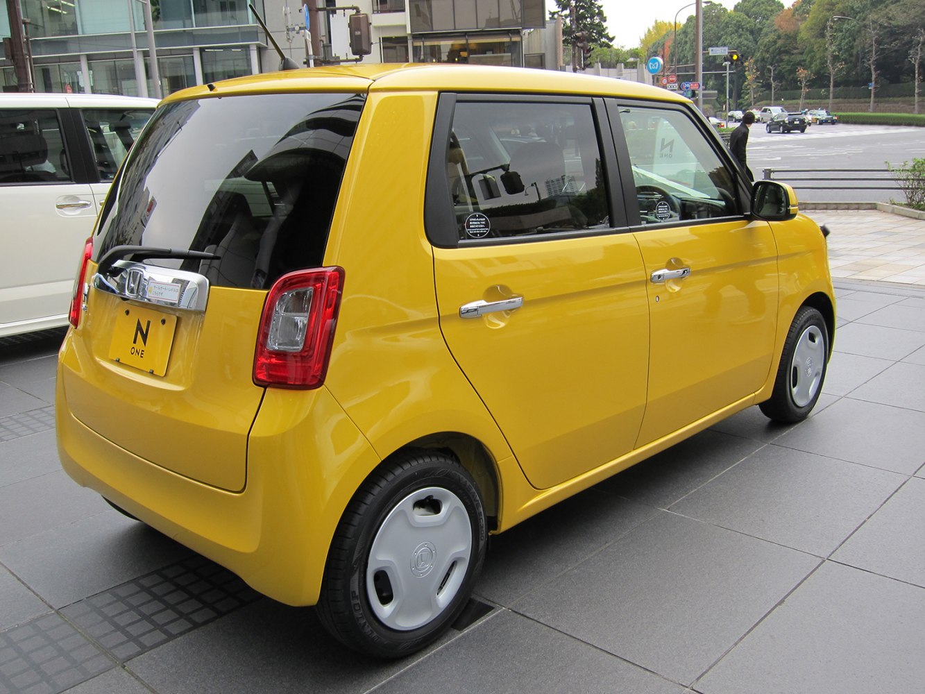 Compact yellow mini hatchback, rear side view, distinct taillights.