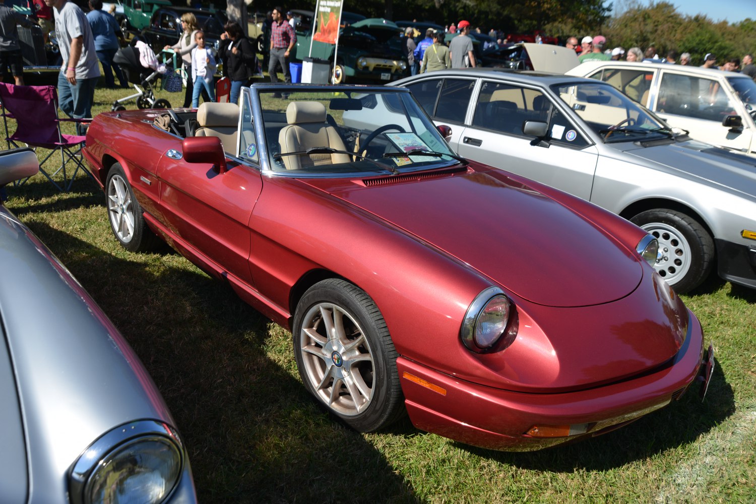 Red convertible with round headlights and sporty wheels on grass.