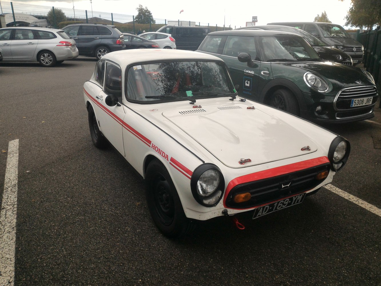 White compact coupe with red racing stripes and hood latches