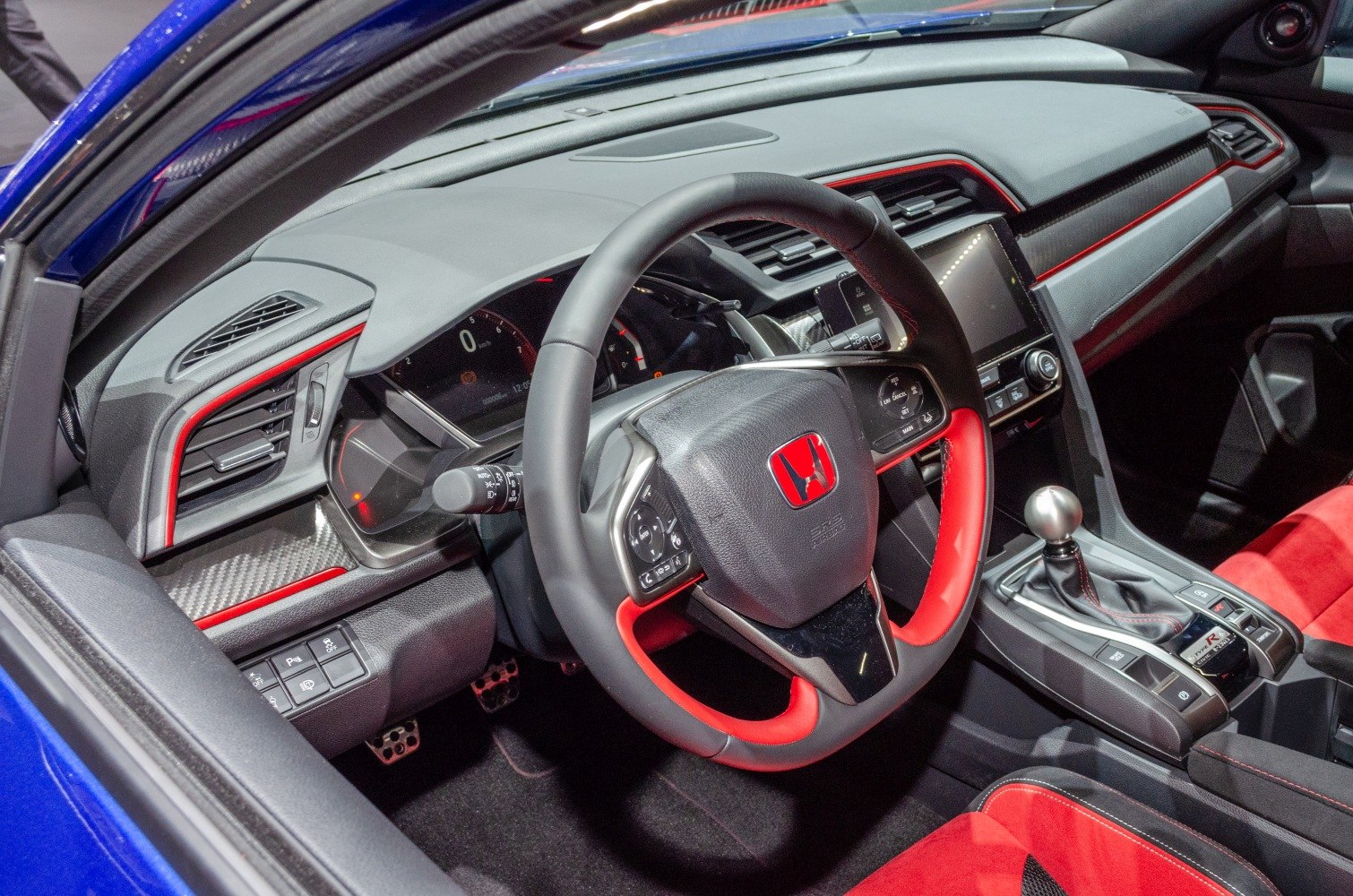 Sporty steering wheel and gearshift knob with red accents inside a car interior.