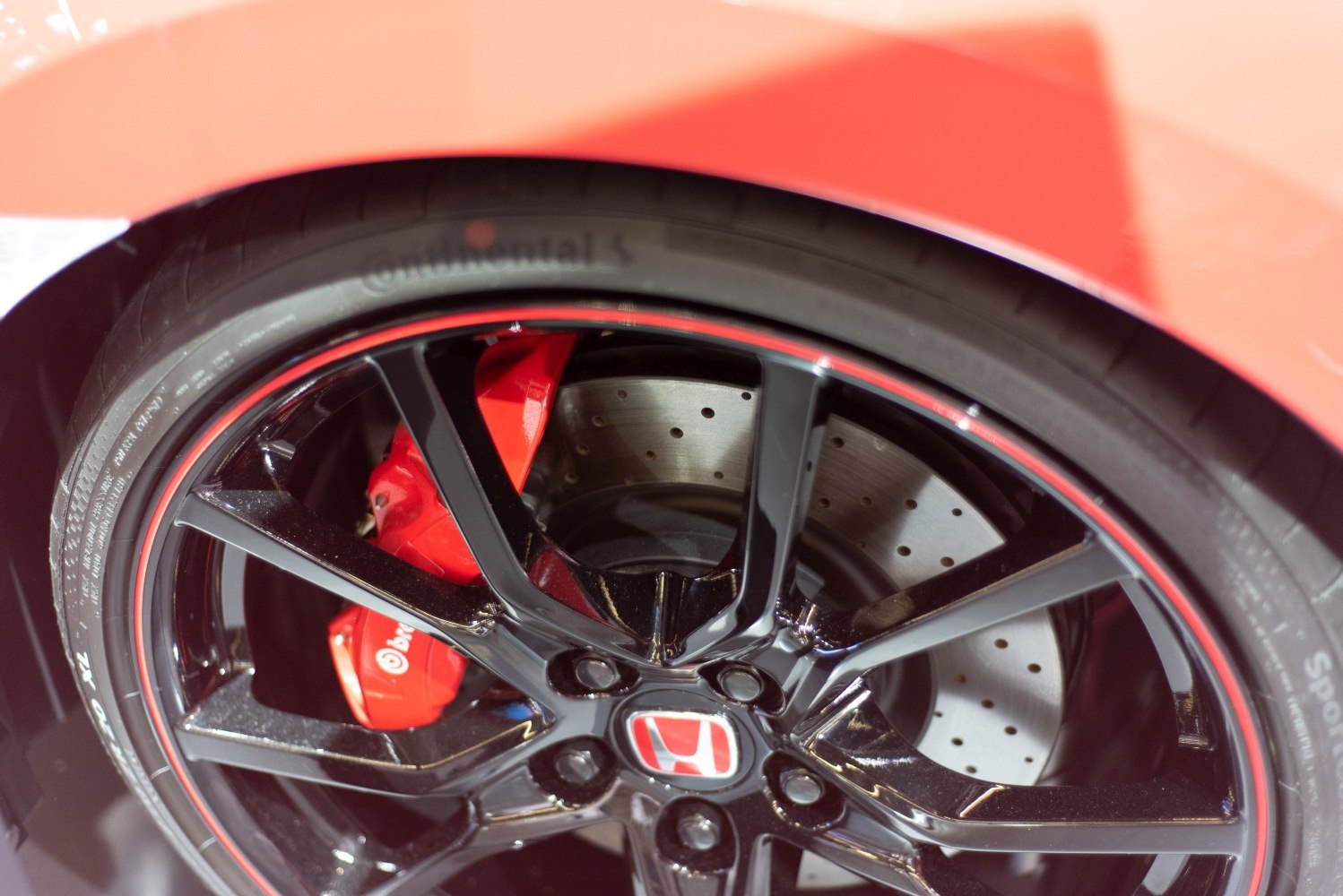 Red Brembo brake calipers with drilled rotors behind black multi-spoke alloy wheel