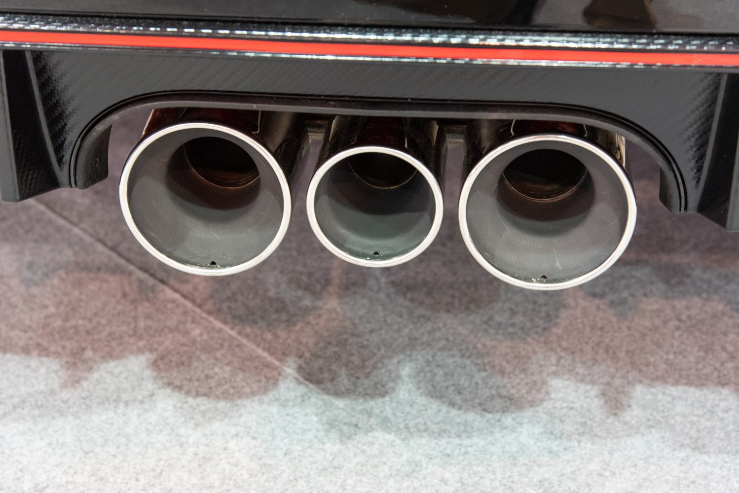 Triple large round exhaust tips with carbon fiber rear diffuser and red accent line.
