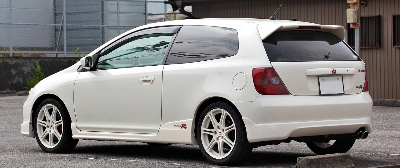 Rear-side view of white hatchback with spoiler and dual exhaust