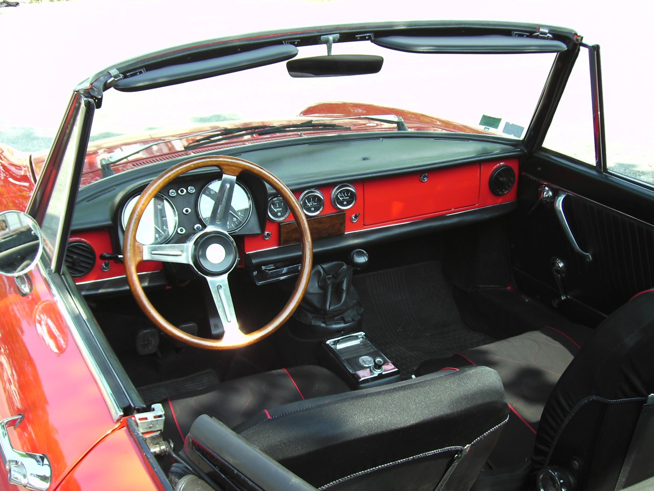 Classic convertible interior with wooden steering wheel and red dashboard