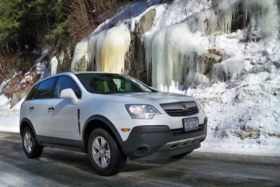 Silver SUV with black trim on snowy icy road near frozen cliffs