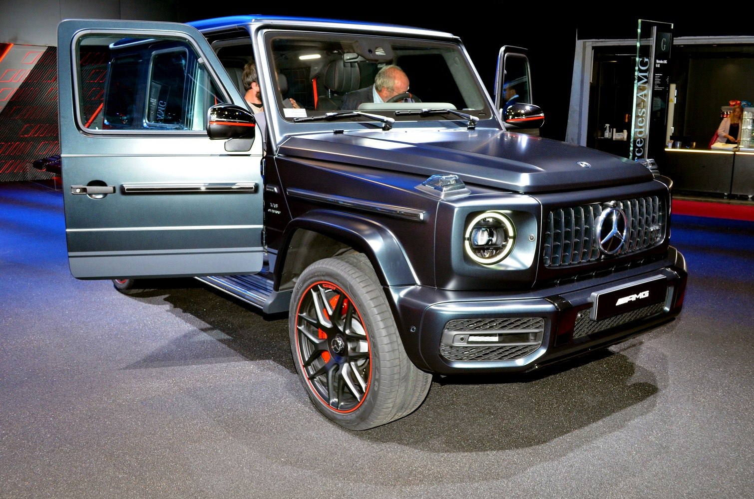 Front view with open door, round LED headlights, AMG grille and black wheels with red calipers