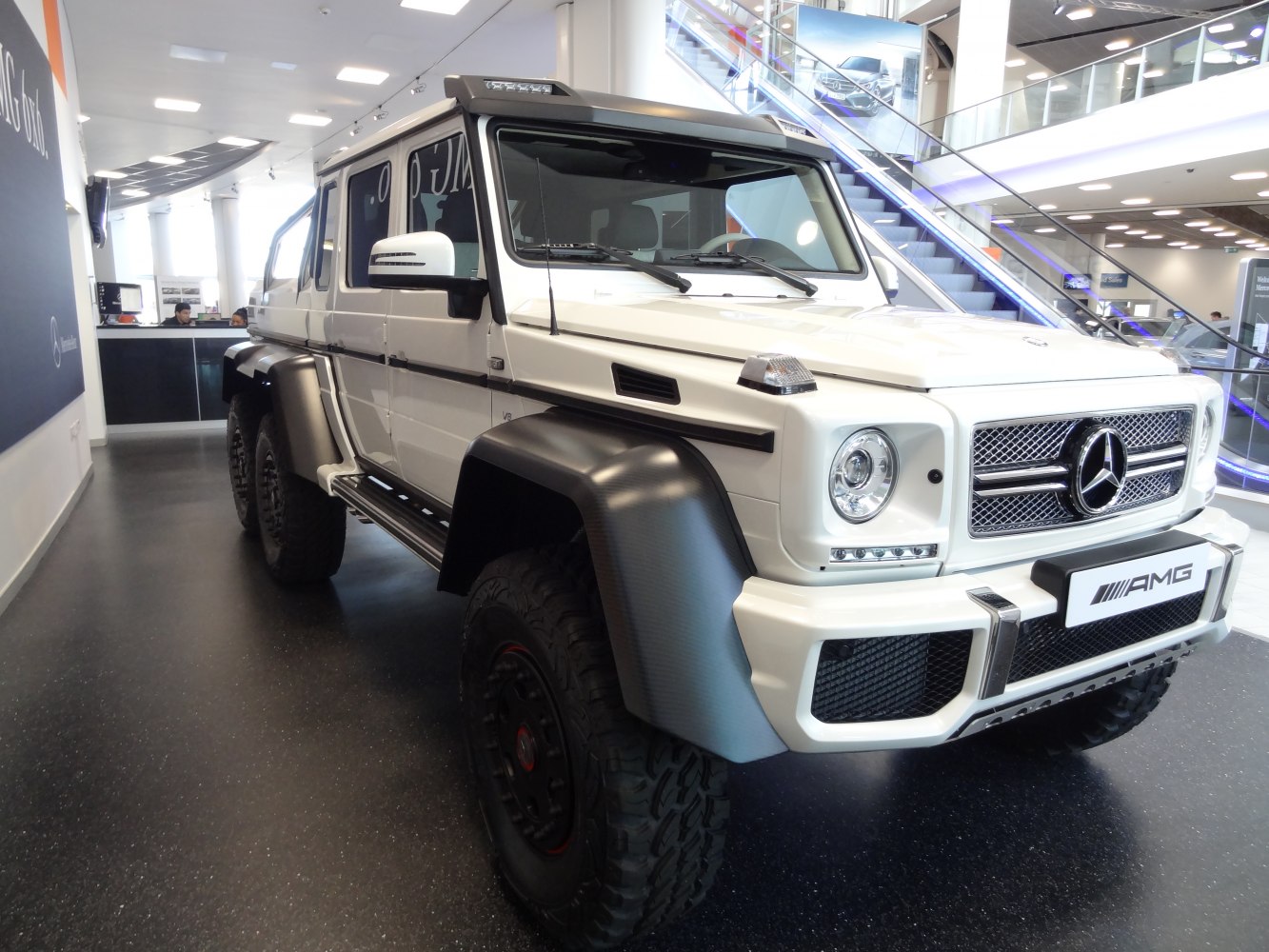 Rugged white 6x6 SUV with large tires and AMG styling in modern showroom