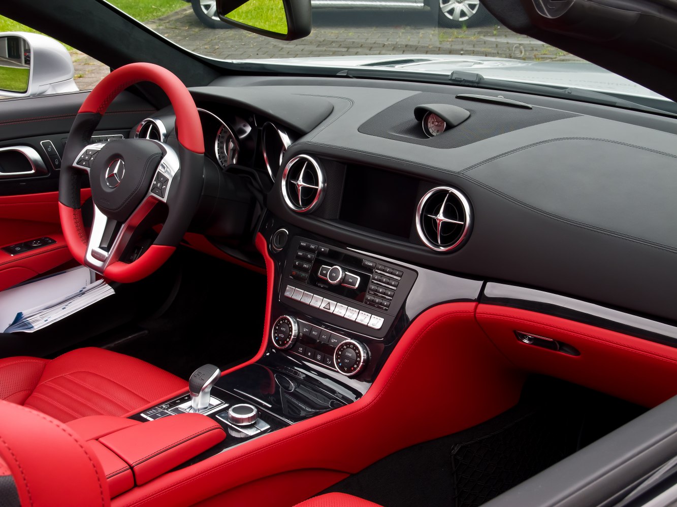 Luxury car interior with red and black leather, sporty steering wheel and dashboard.