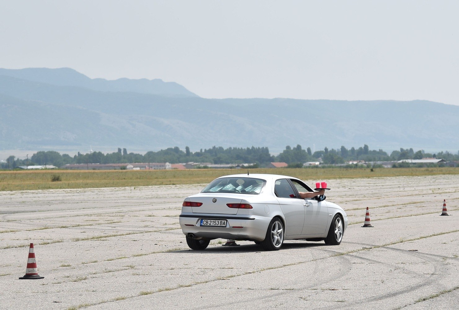 Rear view of white sedan on track with arm holding tray carrying red cups