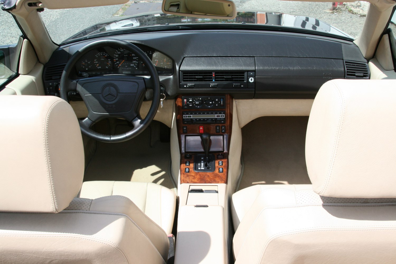 Beige leather seats and wood-trimmed dashboard with analog gauges and center console in vintage sports coupe.