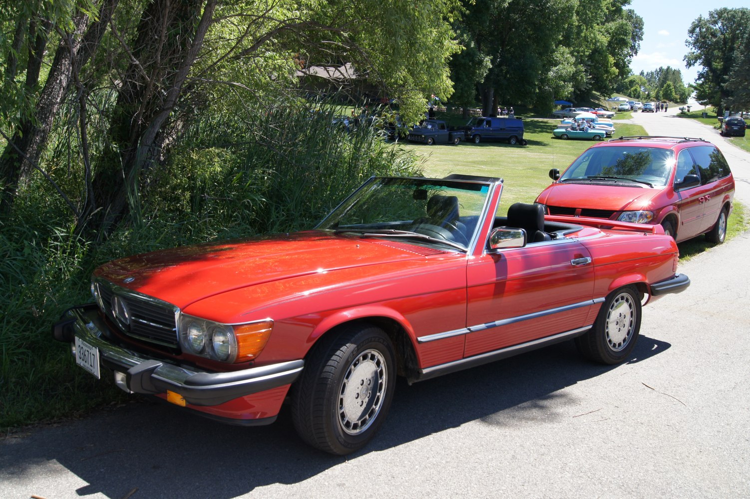 Red convertible roadster with classic alloy wheels near greenery.