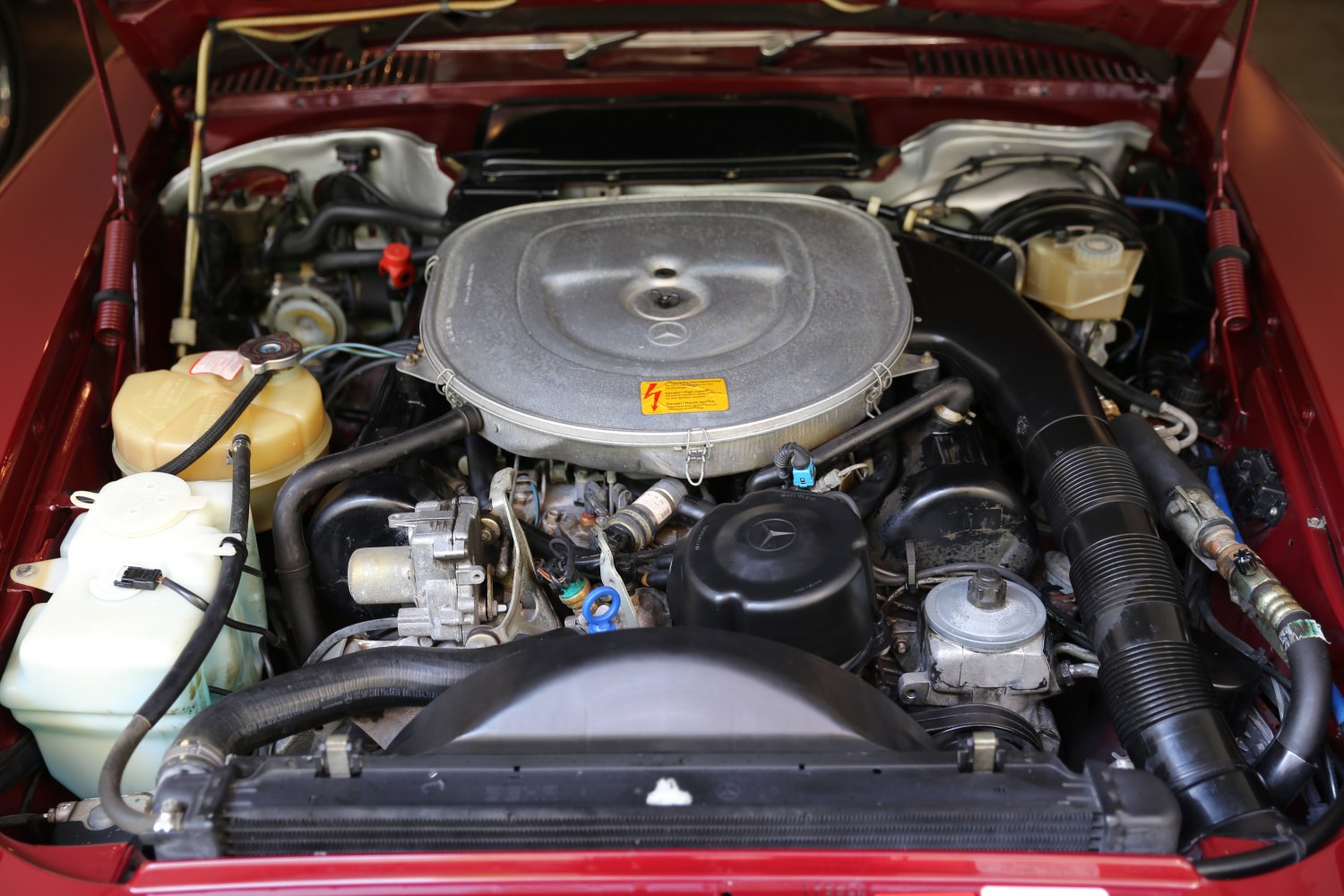 Classic car engine bay with large round air filter and engine components