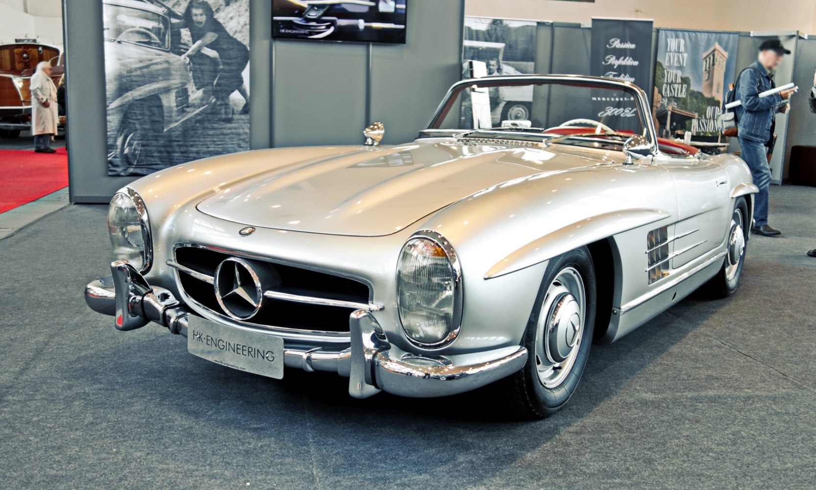 Silver vintage roadster with chrome grille, round headlights, and convertible design.