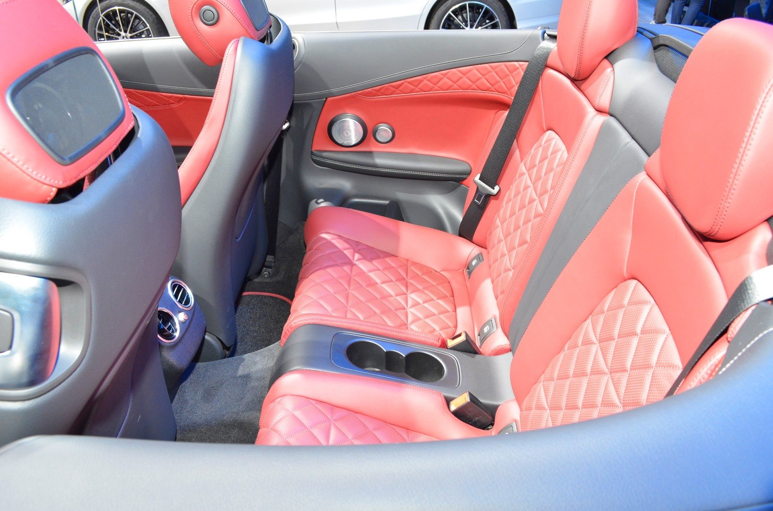 Red quilted leather rear seats with cup holders and door panel in convertible car interior.