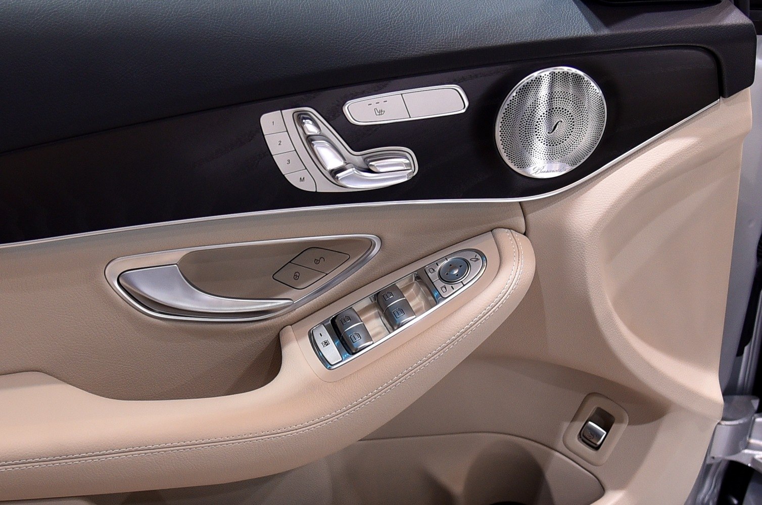 Beige car door panel with seat adjustment controls and premium speaker grille