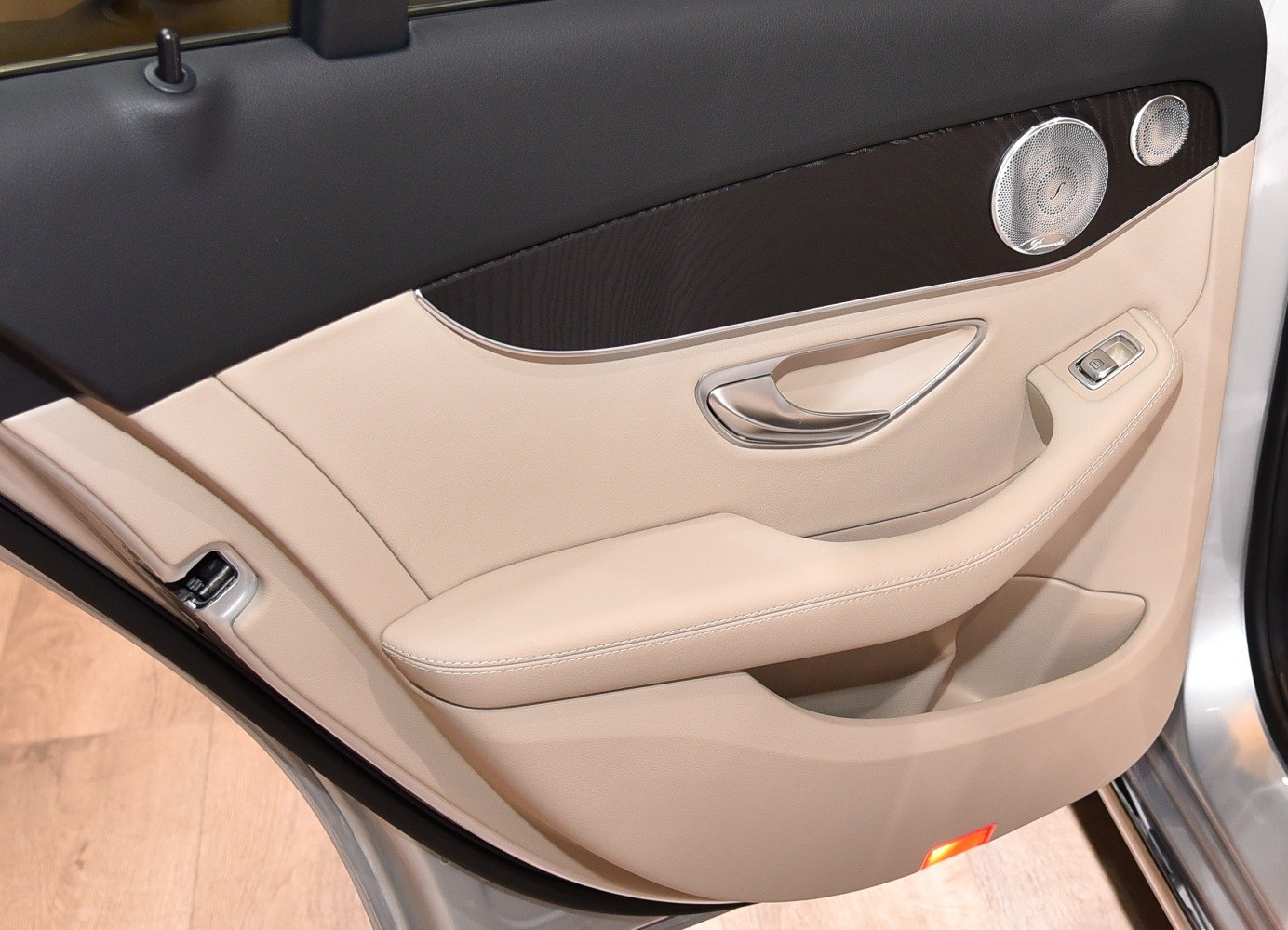 Beige leather car door with wood trim, chrome handle, and speaker