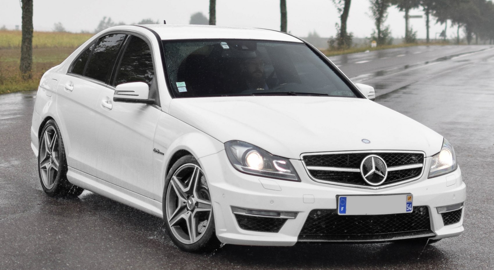 White sedan with AMG wheels and aggressive front grille in rain