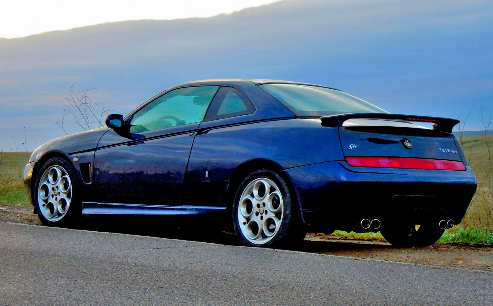 Sleek coupe rear side with spoiler, alloy wheels, and quad exhaust tips