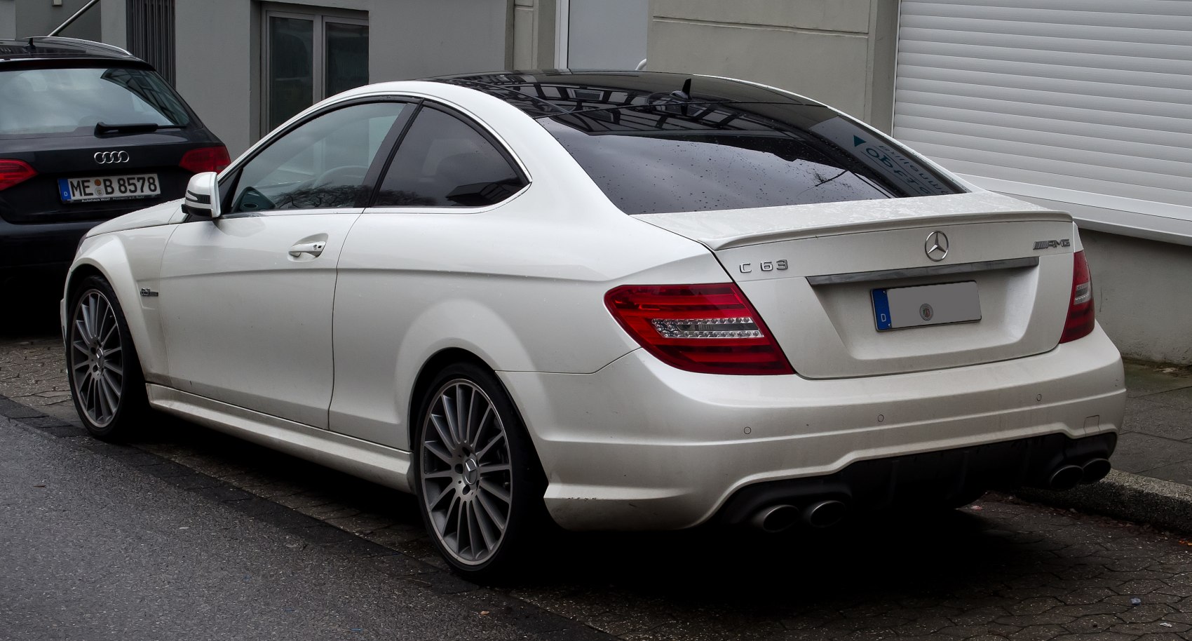 White coupe with quad exhausts, rear spoiler, and multi-spoke wheels