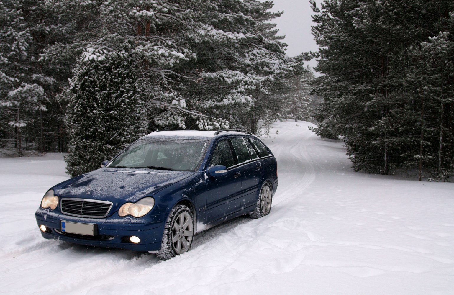 Blue station wagon driving in a snowy forest road