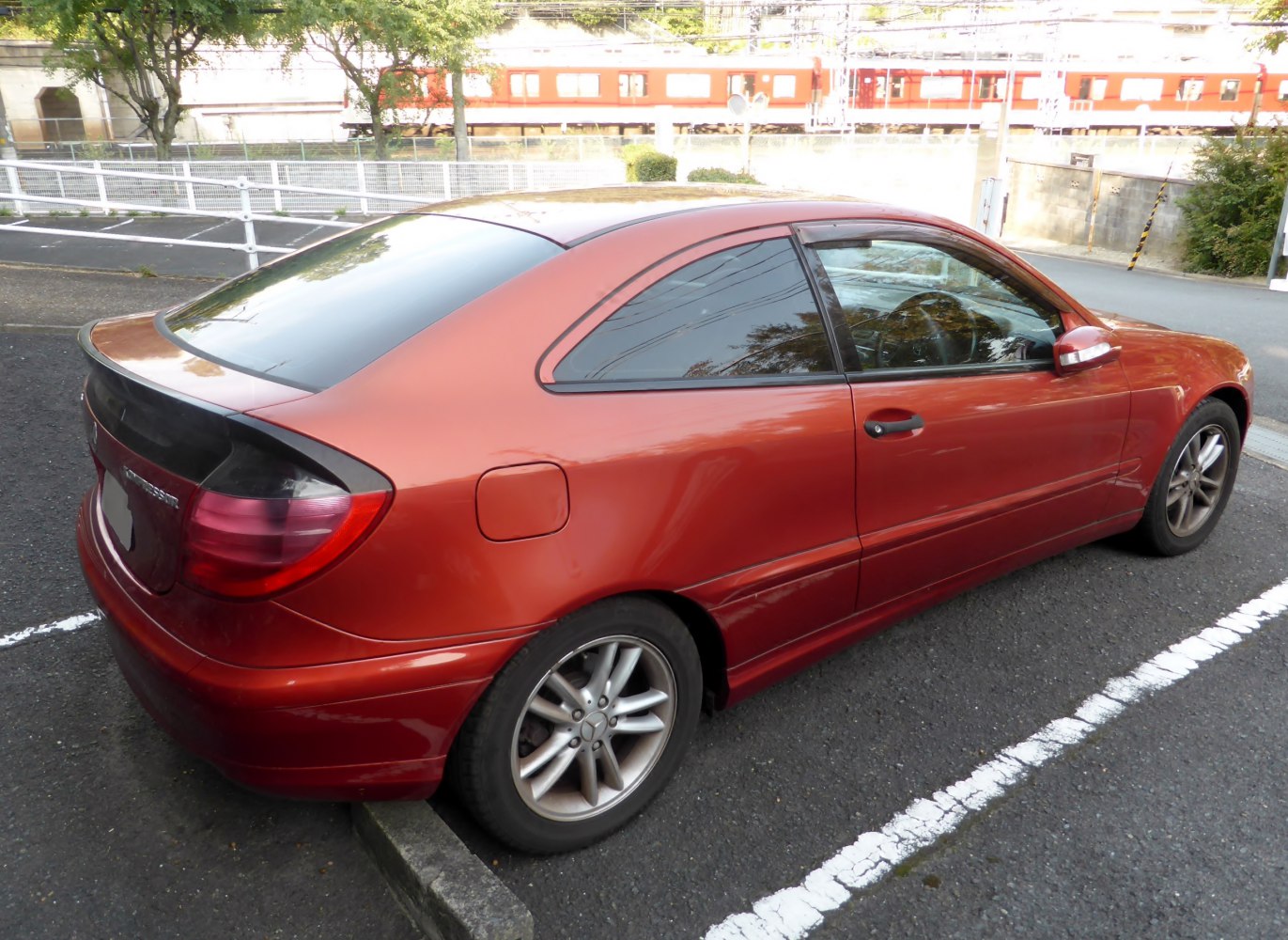 Rear side view of a red sport coupe with alloy wheels parked outdoors