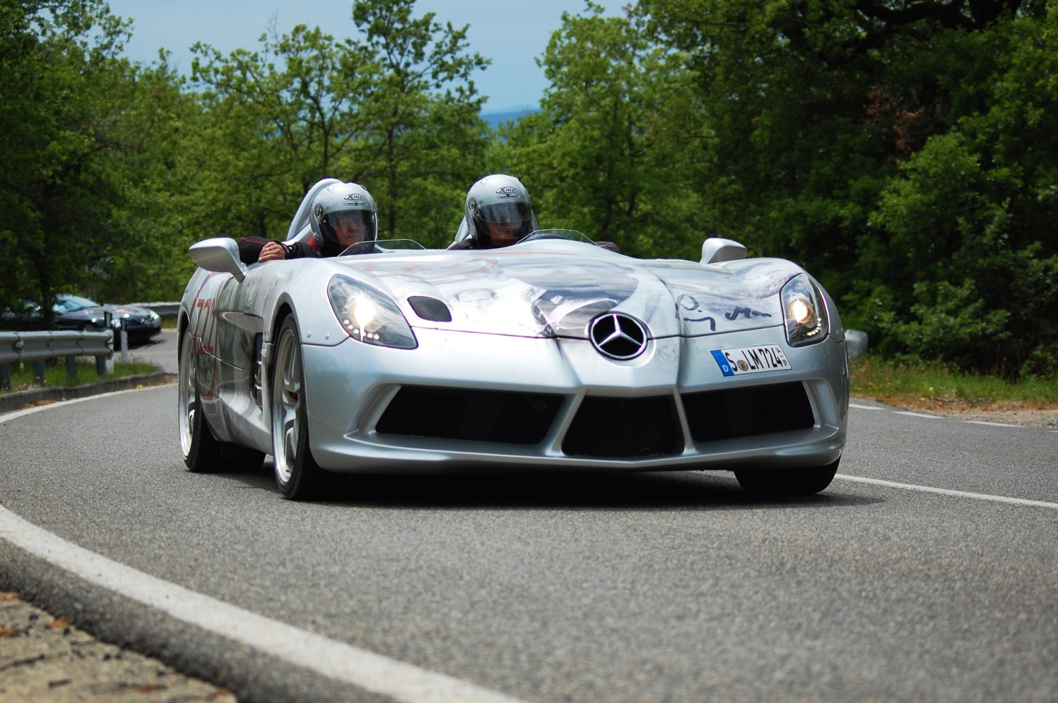 Silver open cockpit sports car with aerodynamic front and two helmets.
