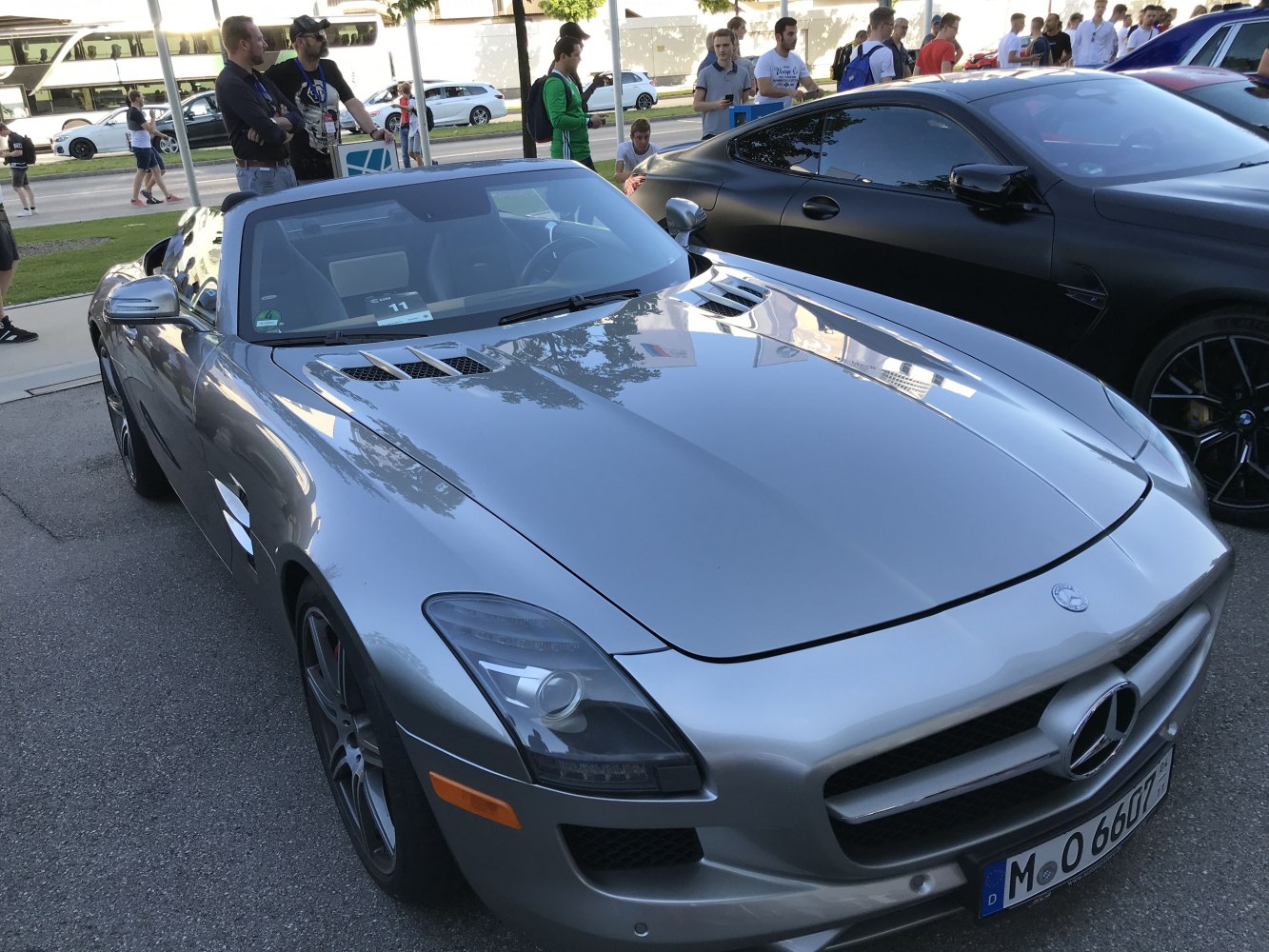 Front and side view with prominent grille and hood vents of a luxury roadster.