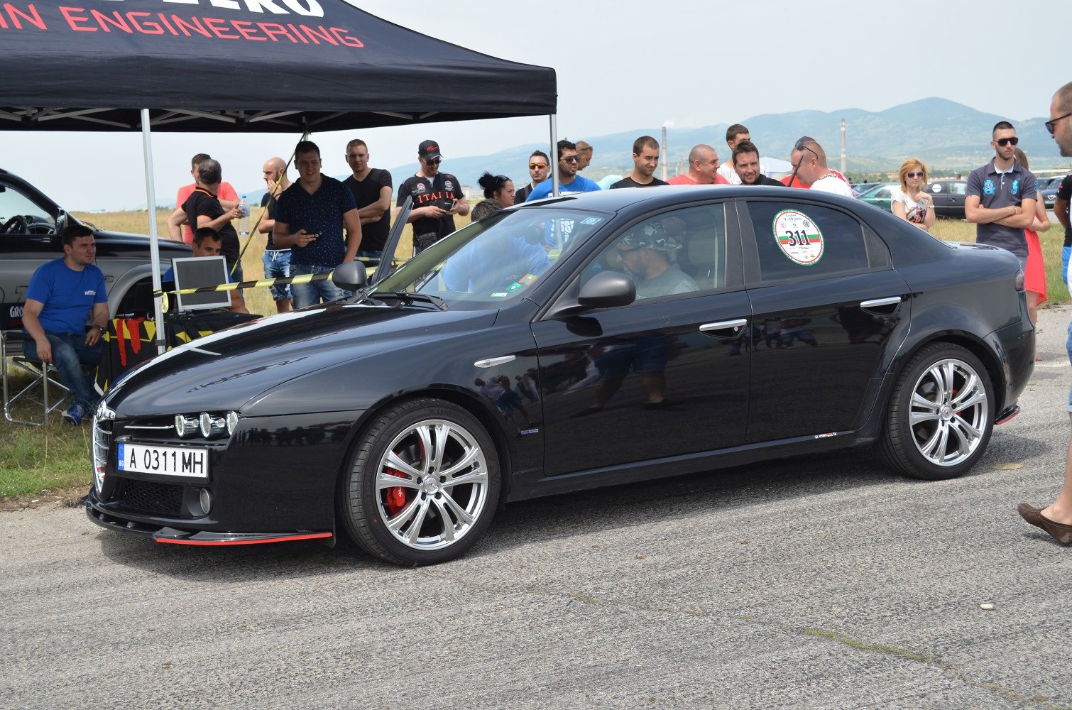 Sporty black sedan with red brakes and multi-spoke wheels at motorsport event