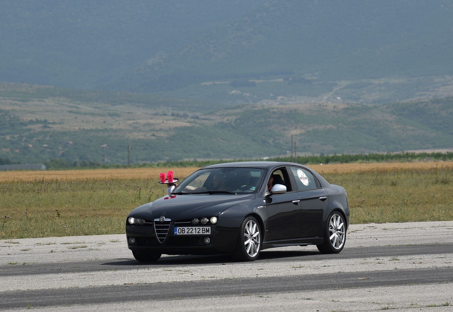 Black sedan with distinctive front grille and alloy wheels on open paved area