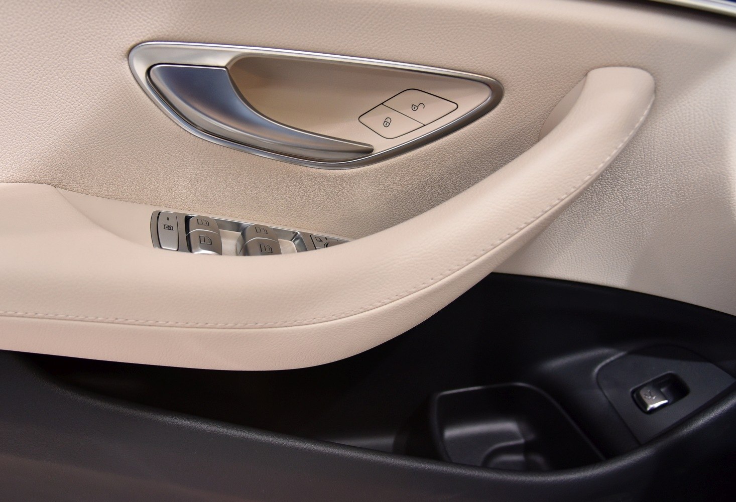 Close-up of beige leather door panel with handle and control buttons