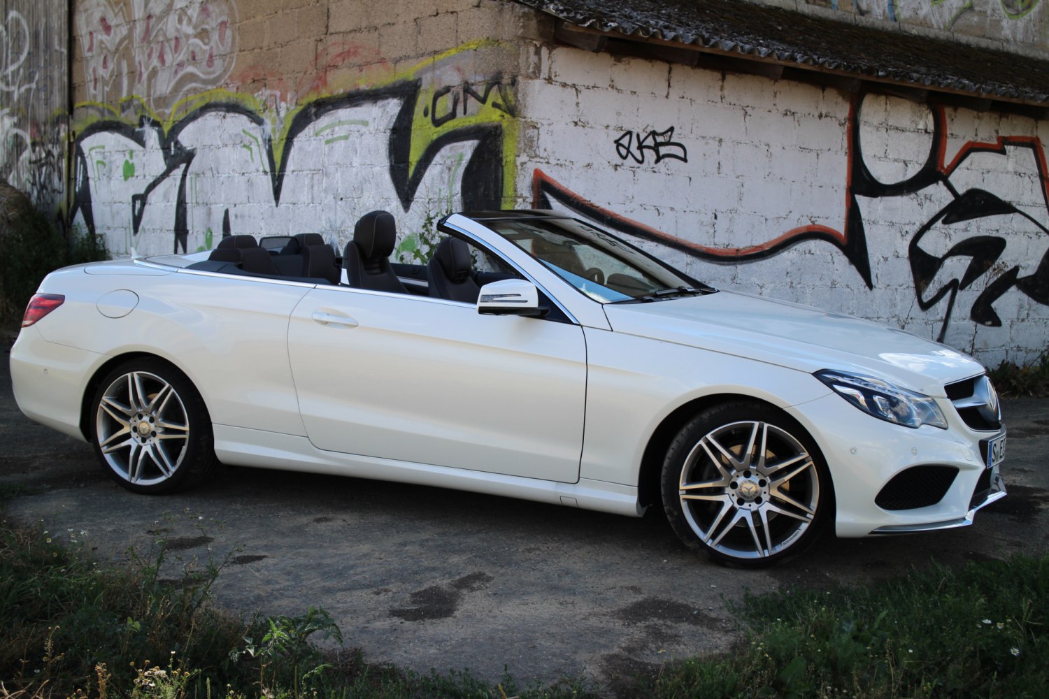 White convertible with alloy wheels and open roof in urban graffiti setting