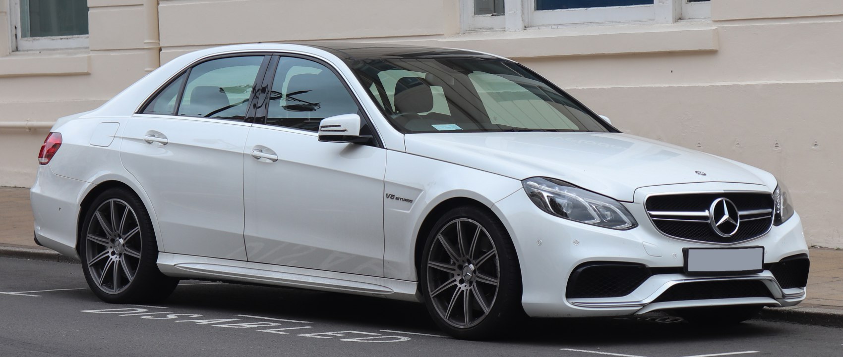 White Mercedes-Benz sedan with V8 Biturbo and AMG wheels parked by sidewalk