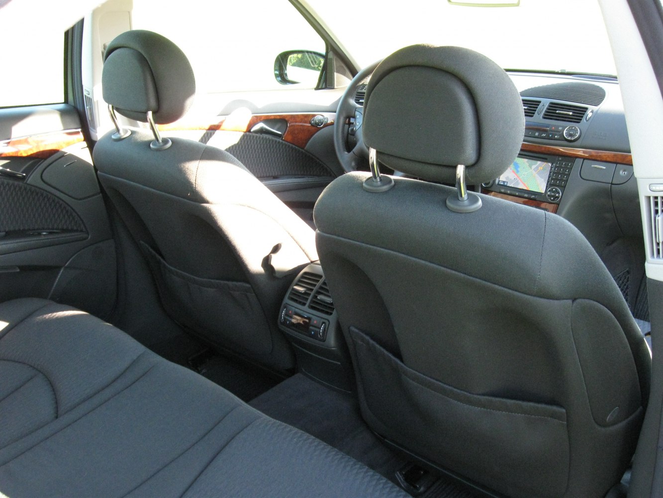 Rear seat interior with cloth upholstery, wooden trim, and dashboard navigation system.