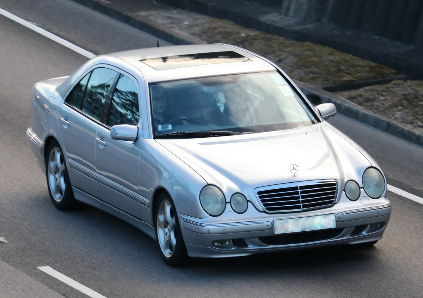 Silver sedan with dual round headlights and sunroof driving on road