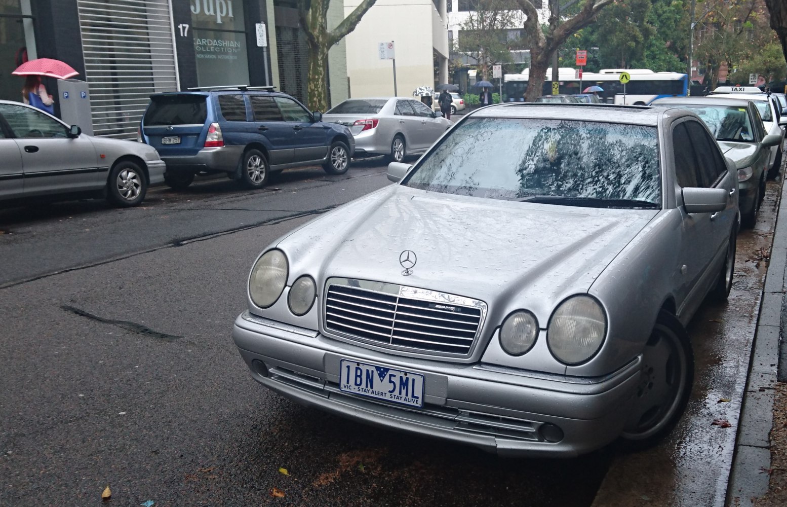 Twin round headlights and chrome grille of a classic sedan in rainy conditions