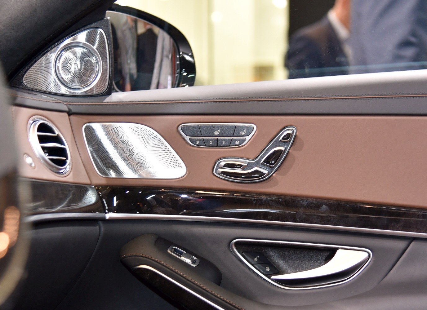 Luxury car door interior with leather trim, seat controls, and premium speaker grills
