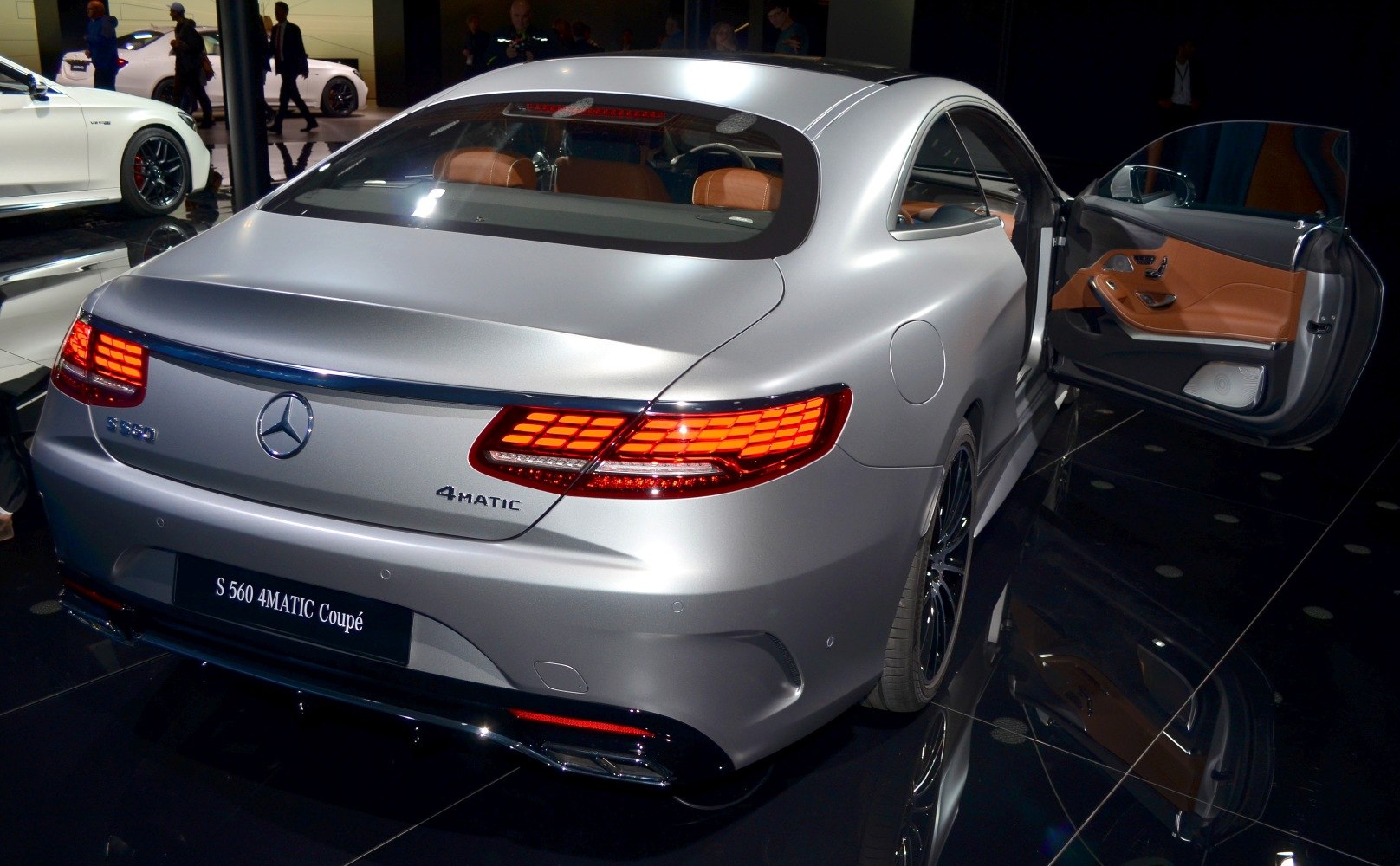Matte silver luxury coupe rear with illuminated LED taillights and open door brown leather interior.