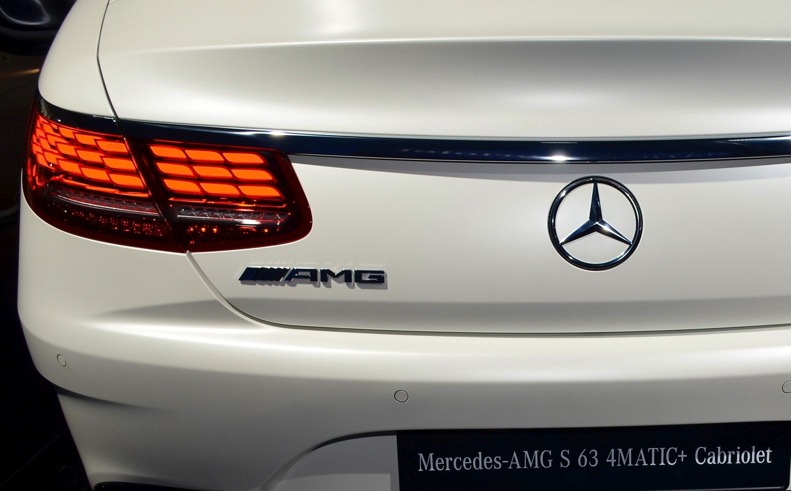 Rear AMG badge and illuminated tail lights on white luxury coupe