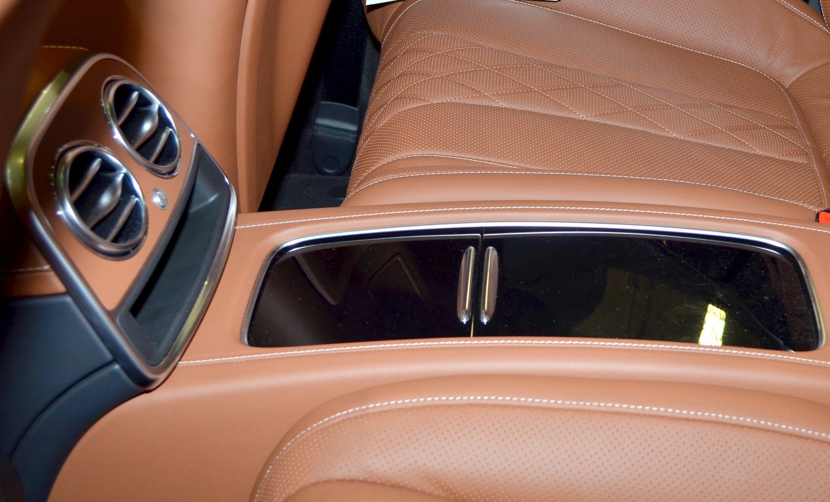 Rear seat center console with air vents and detailed tan leather upholstery.