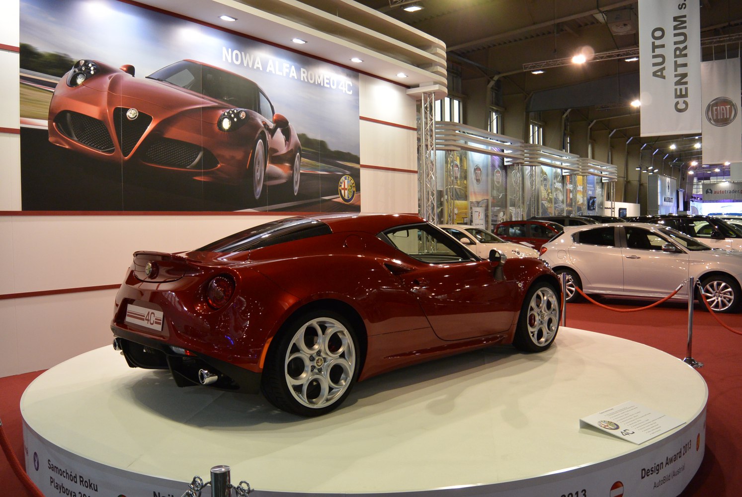 Rear and side profile of a red sports coupe on display platform