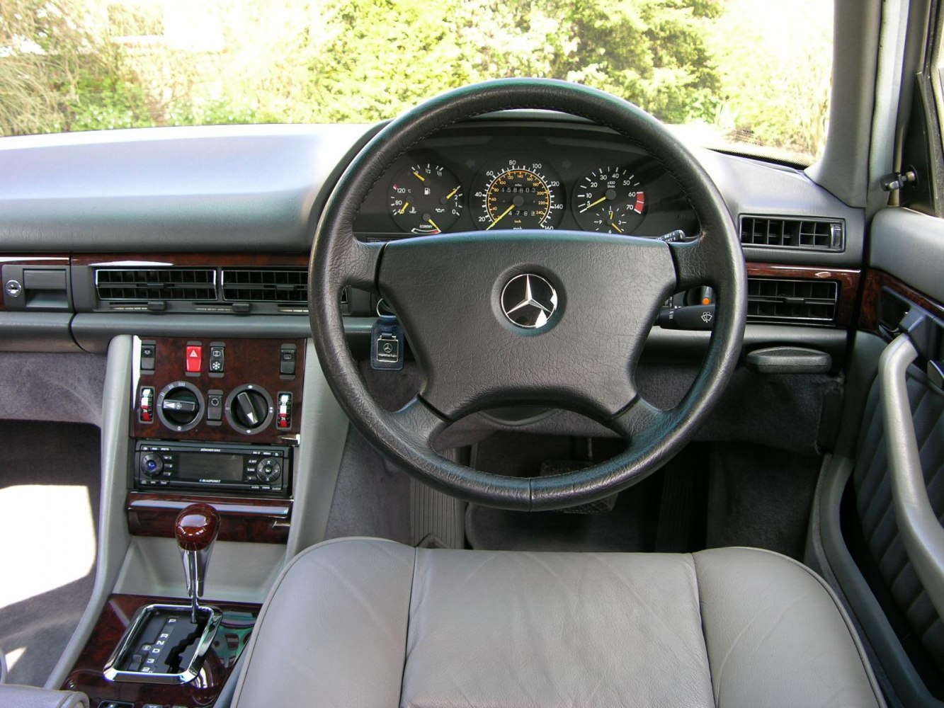 Vintage steering wheel and dashboard with wood panel accents and automatic gearshift.