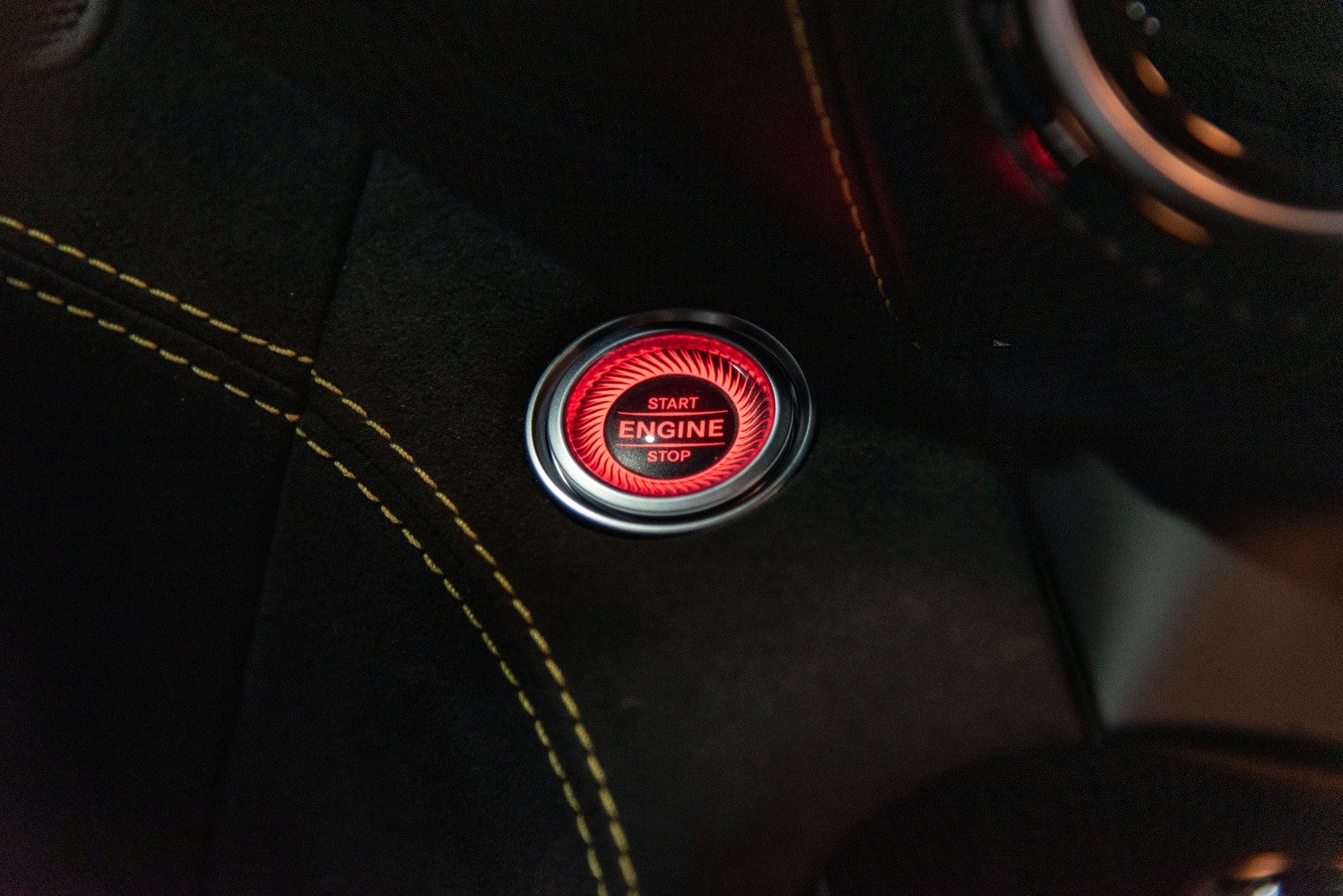 Illuminated red engine start/stop button with yellow contrast stitching interior
