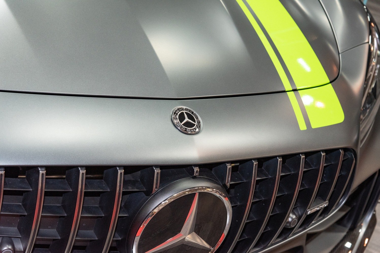 Close-up of AMG GT hood emblem with yellow racing stripes and vertical grille bars