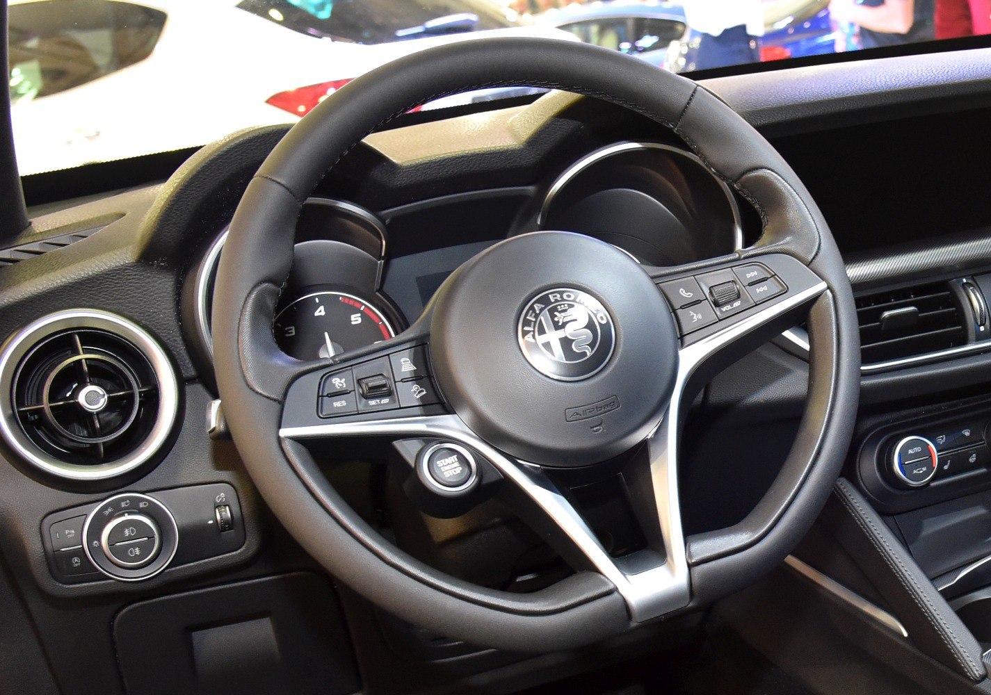 Steering wheel with control buttons and dashboard featuring start/stop button.